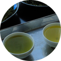 Two small white bowls filled with pale yellow-green liquid, set on a reflective metal surface with a dark tray in the background.
